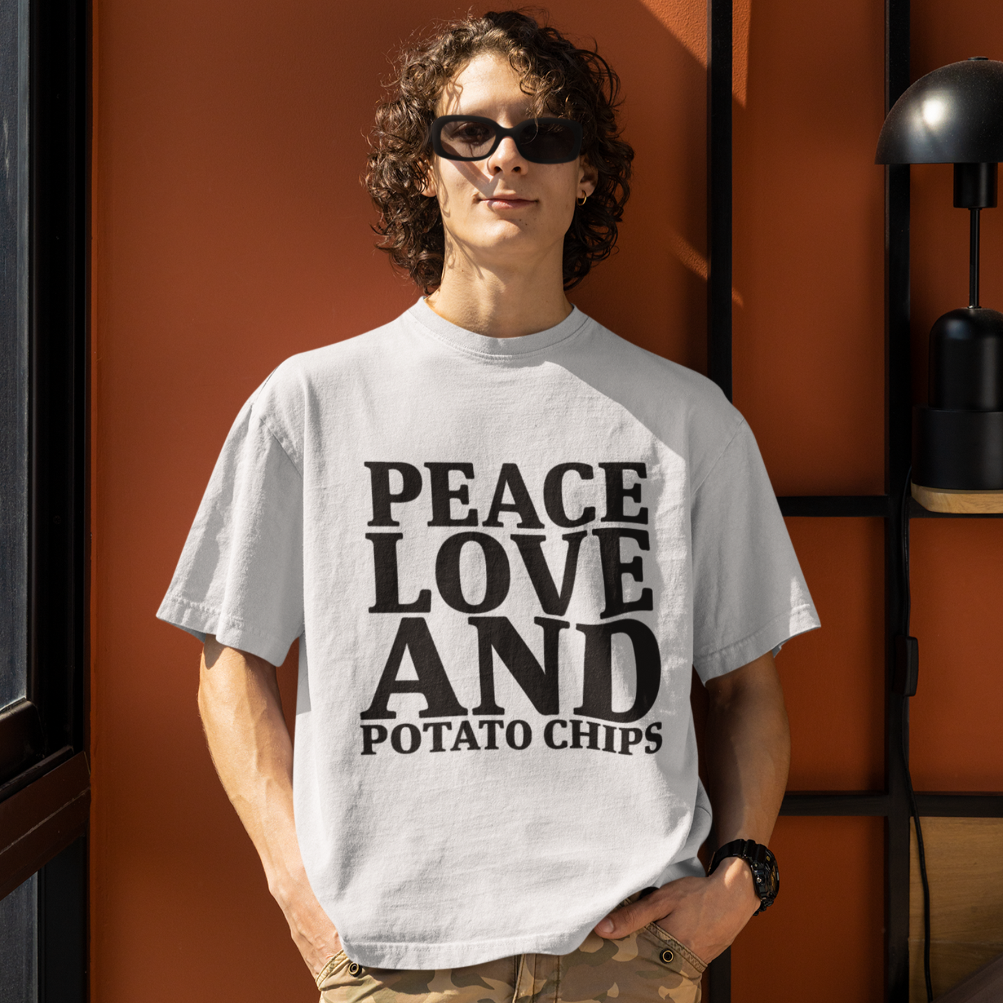 Person wearing a t-shirt with 'Peace Love and Potato Chips' text against an orange wall.