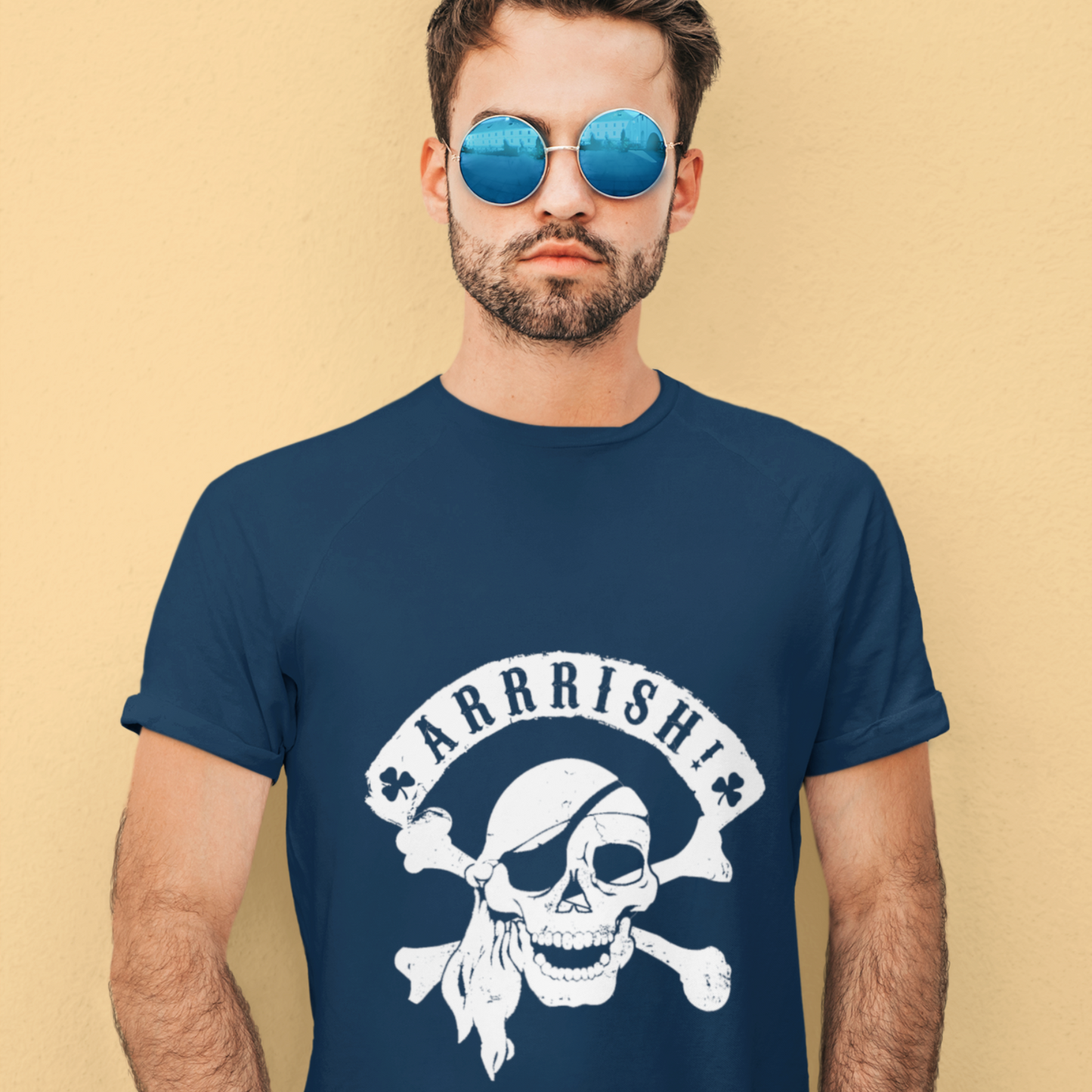 Man wearing a navy blue t-shirt with a skull and crossbones design and 'ARRRISH!' text on a beige background.