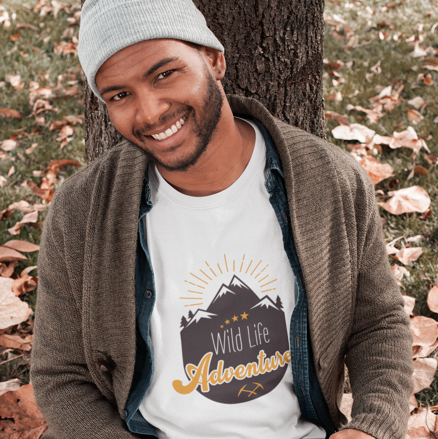 Man sitting on the ground with an open book, wearing a t-shirt with 'Wild Life Adventure' design.