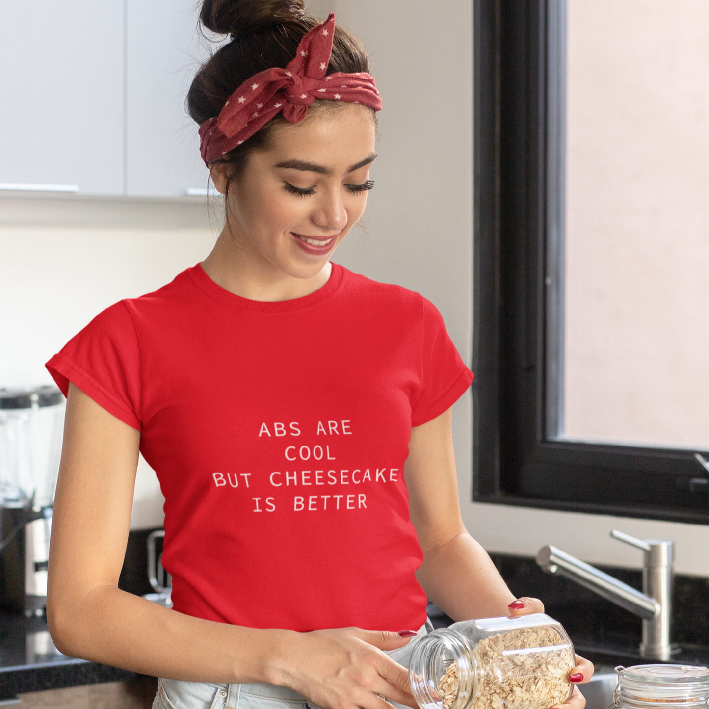 Woman in a kitchen wearing a red t-shirt with text, preparing food.
