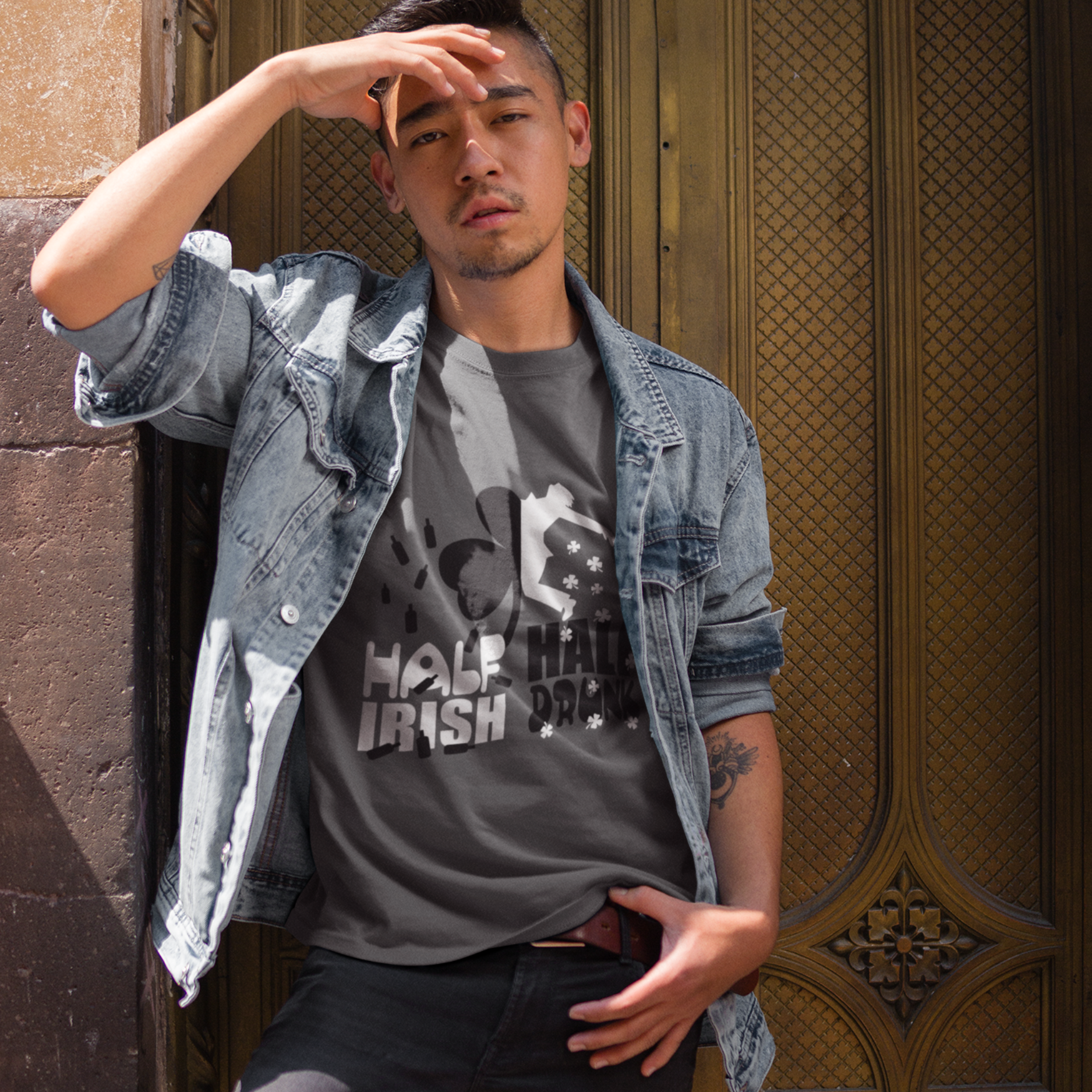 Man wearing a gray t-shirt with text and denim jacket against a textured wall.