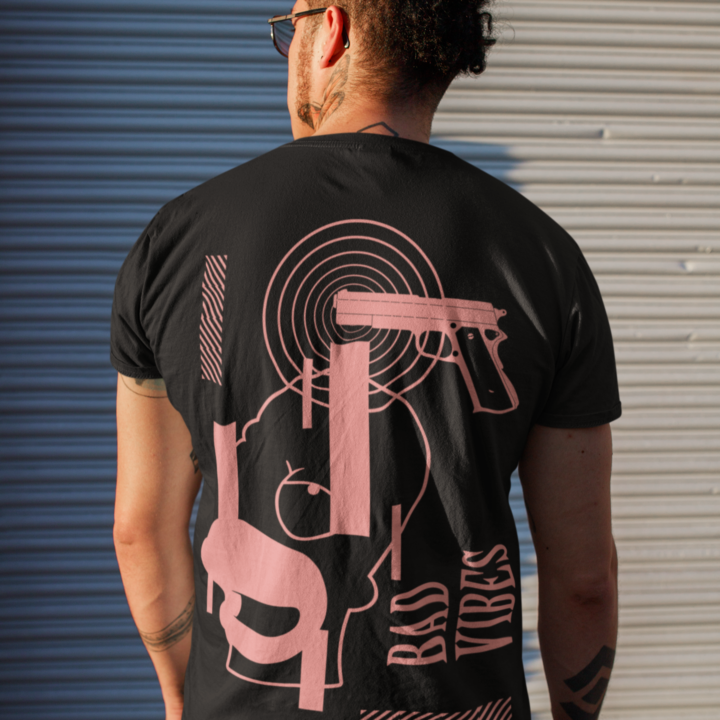 Person wearing a black t-shirt with pink graphic design against a metallic shutter background