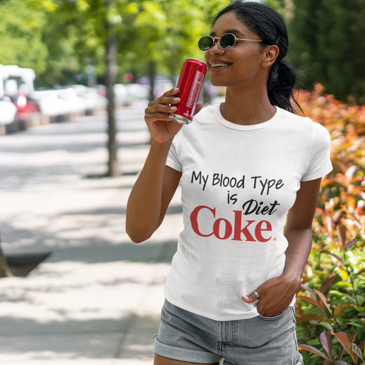 Person wearing a t-shirt with 'My Blood Type is Diet Coke' text, holding a Diet Coke can outdoors.