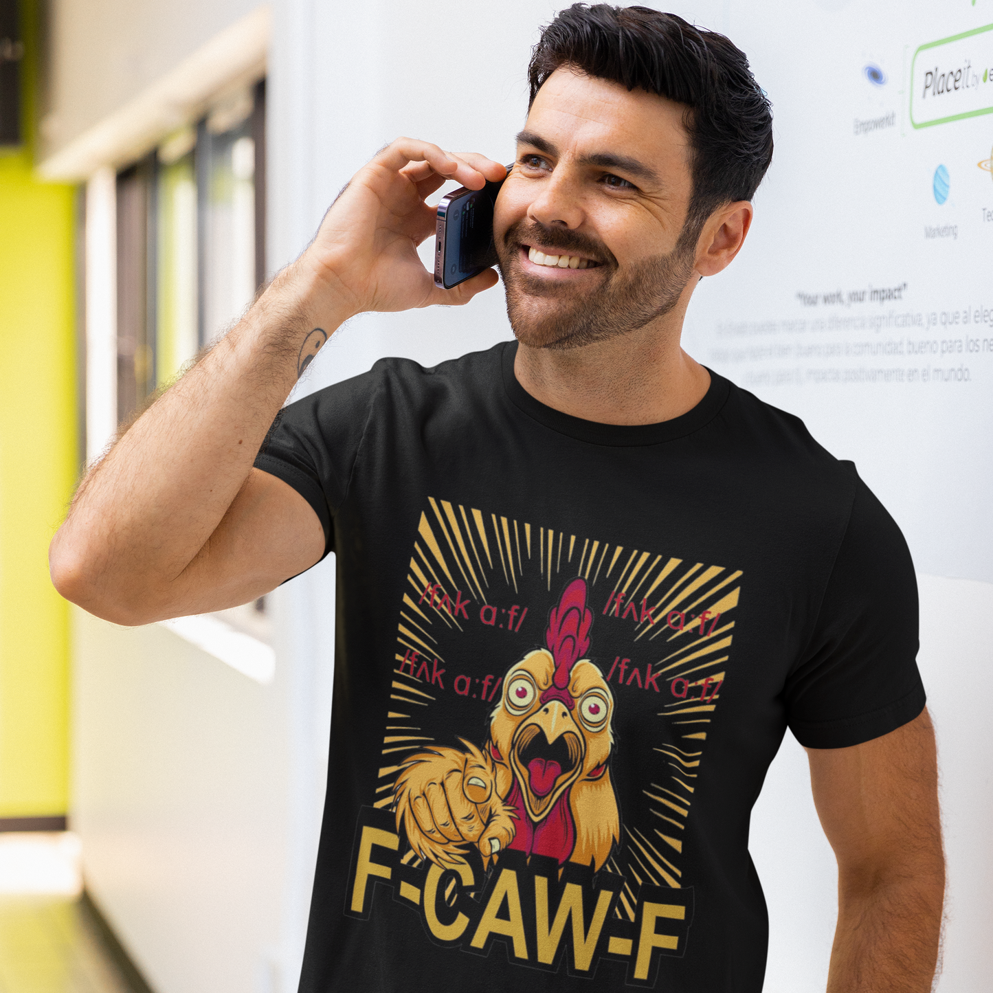 Man wearing a black t-shirt with a graphic design and text, talking on a phone in an indoor setting.