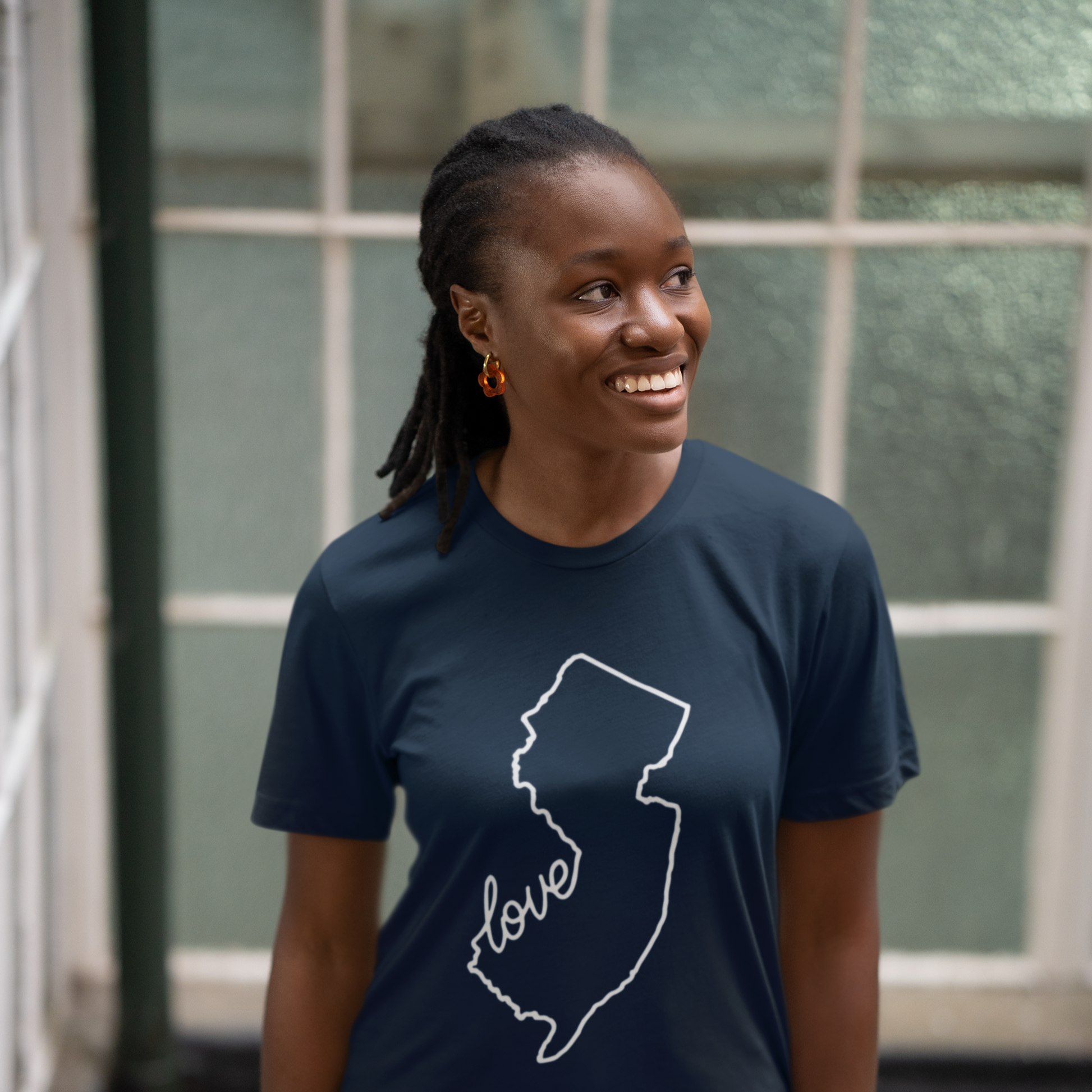Person wearing a navy blue t-shirt with a white outline of a state and the word 'love' inside it, standing indoors.