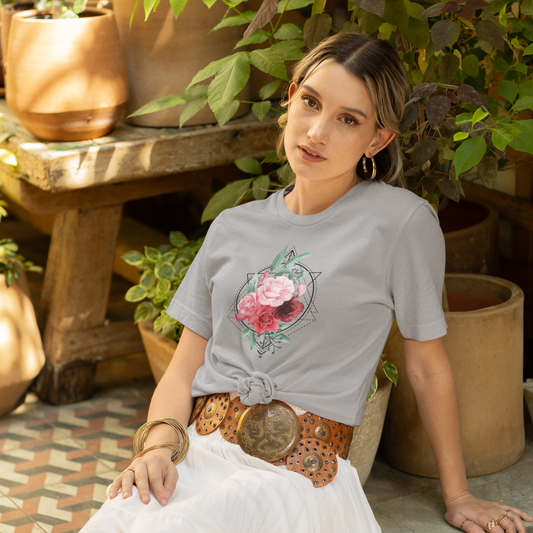 Woman wearing a gray t-shirt with a floral design, sitting outdoors among potted plants.