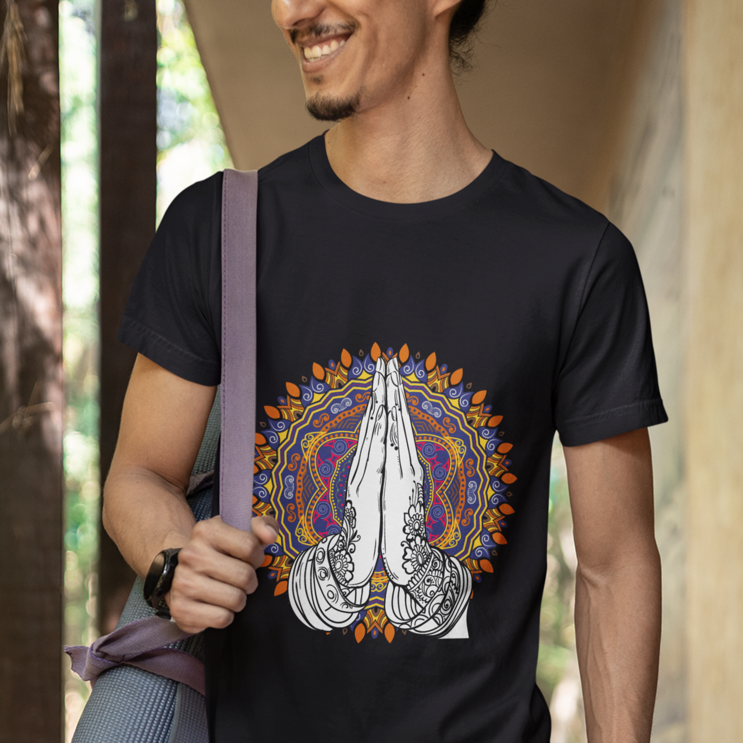 Man wearing a black t-shirt with a colorful design, holding a yoga mat.