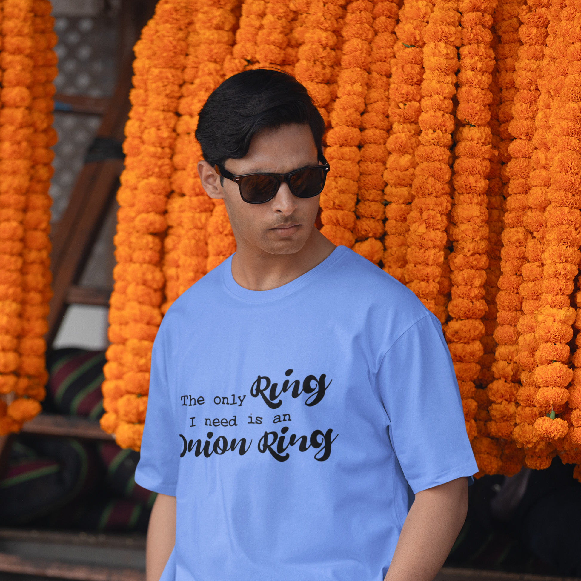 Man wearing a light blue t-shirt with text in front of orange marigold flowers