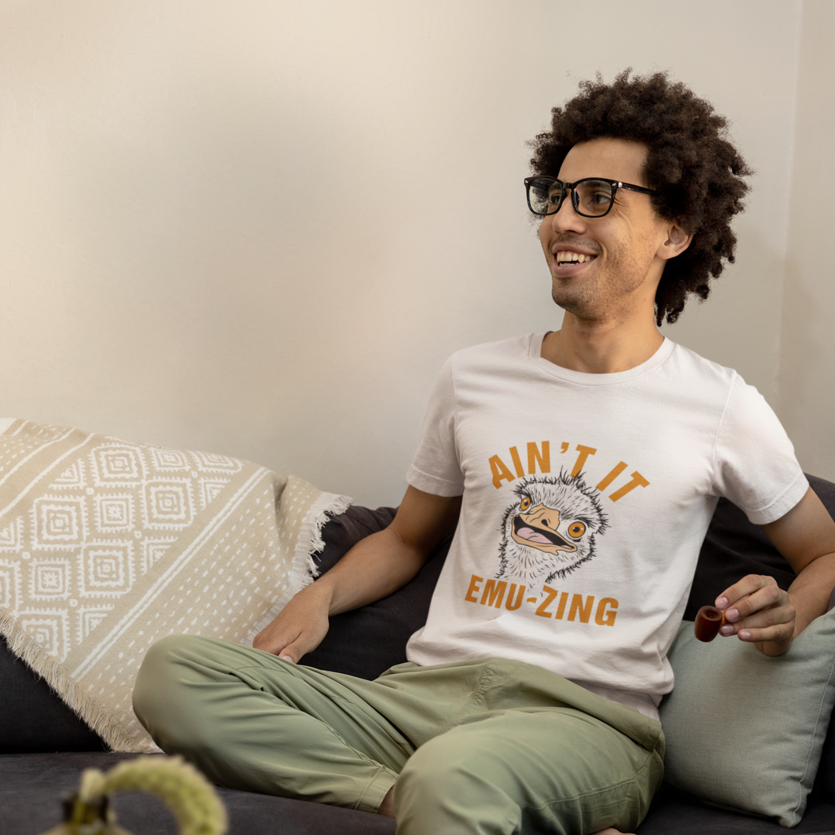Man sitting on a couch wearing a white t-shirt with text and graphics.