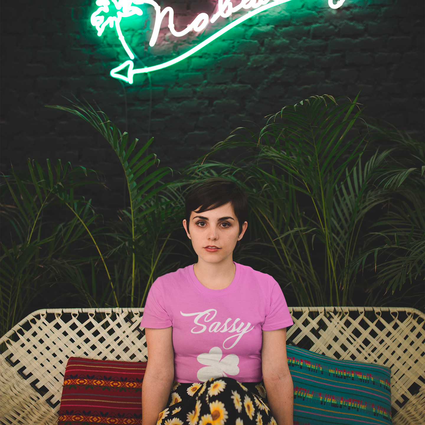Person wearing a pink 'Sassy' shirt sitting on a couch with a neon sign in the background