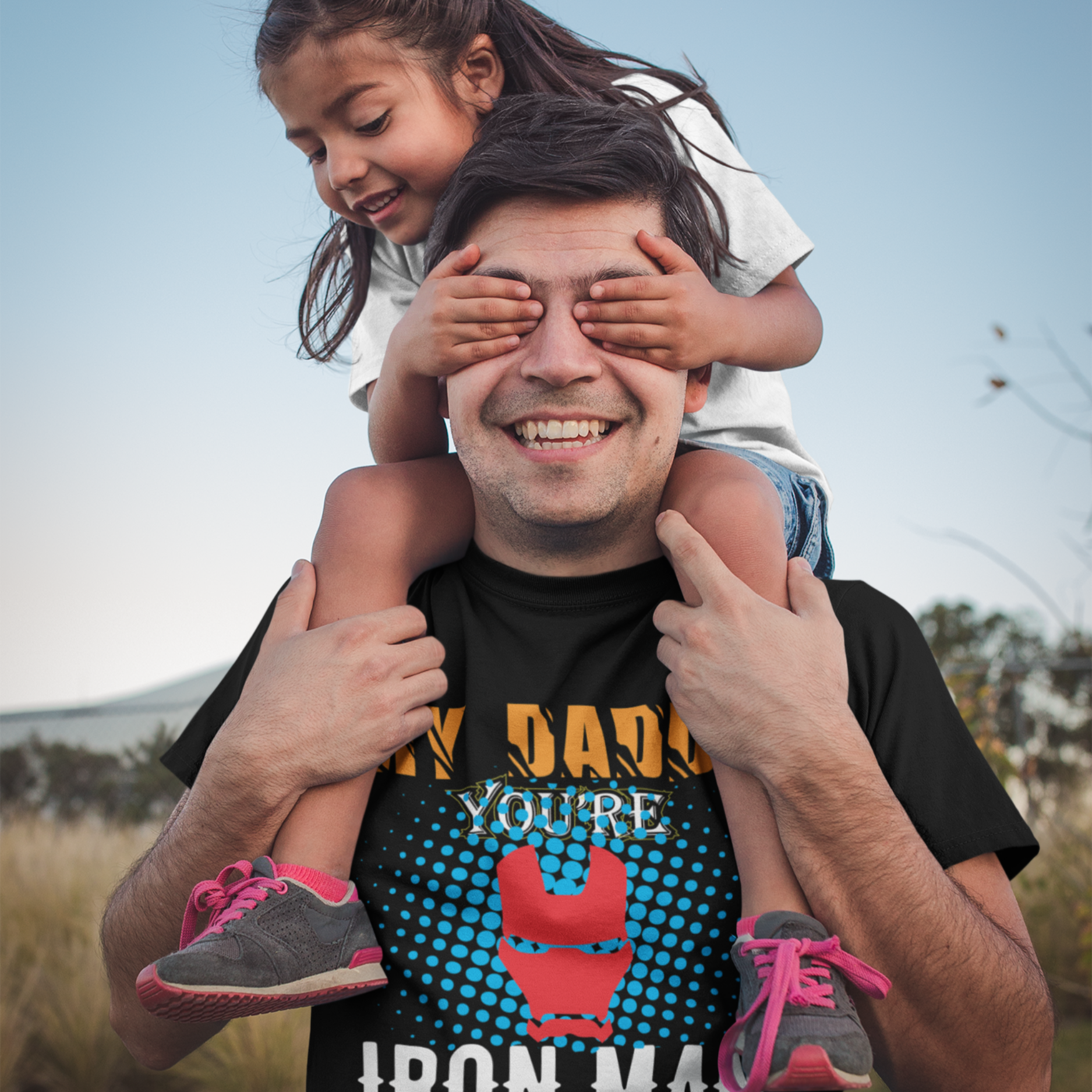 Man with a child on his shoulders, both smiling outdoors.