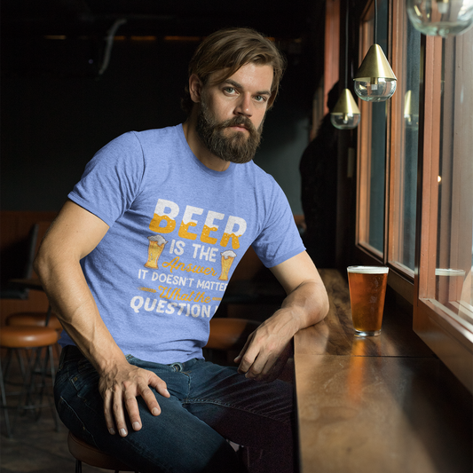 Man sitting at a bar wearing a blue t-shirt with text, holding a beer glass.