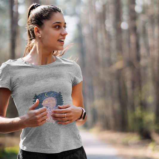 Woman running on a path in a forest wearing a gray t-shirt with a graphic design.