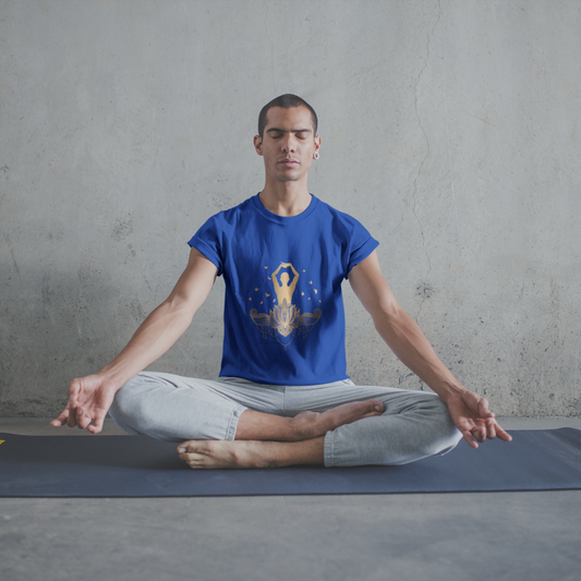 Man in a blue t-shirt and gray pants sitting in a yoga pose on a mat against a plain wall.