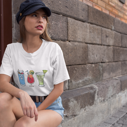 Woman wearing a white t-shirt with colorful drink graphics sitting against a brick wall.