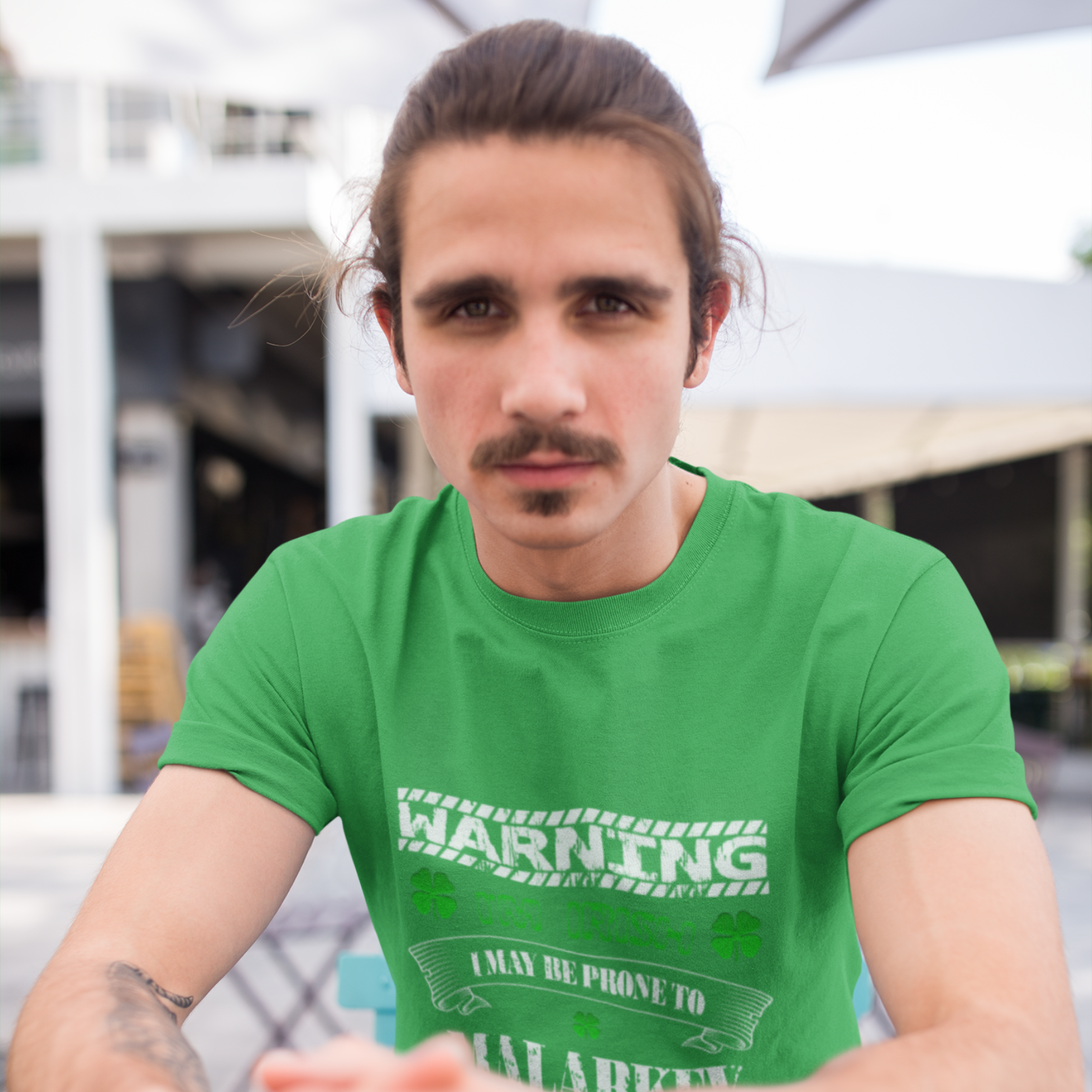 Man wearing a green t-shirt with text sitting outdoors.