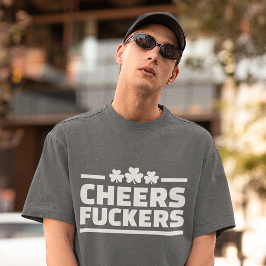 Person wearing a gray t-shirt with 'Cheers Fuckers' text and sunglasses outdoors.