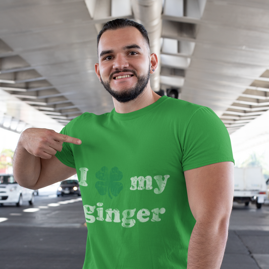 Man wearing a green t-shirt with text, pointing at it, in an outdoor setting.