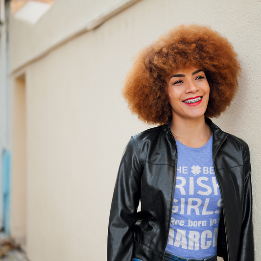 Woman with curly hair wearing a black leather jacket and blue graphic t-shirt on a street.