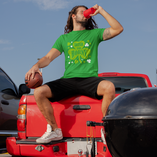 Man in green shirt and black shorts sitting on a red truck, drinking from a red cup.
