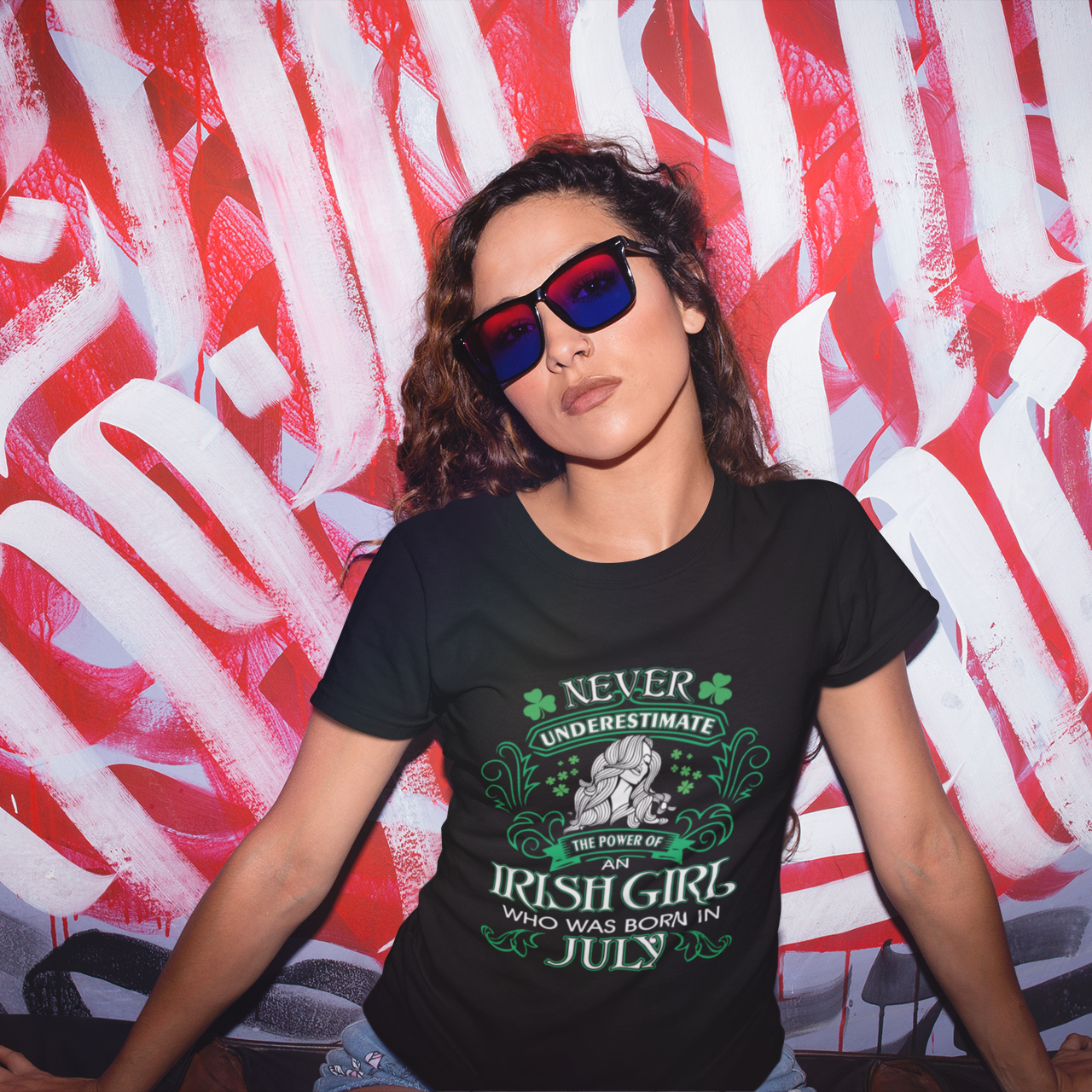 Woman wearing a black t-shirt with text and sunglasses in front of a red and white abstract wall.