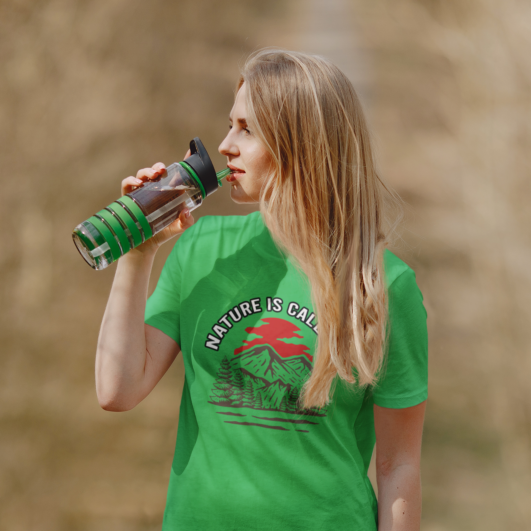 Woman wearing a green t-shirt with 'Nature is Calling' design, holding a water bottle outdoors.