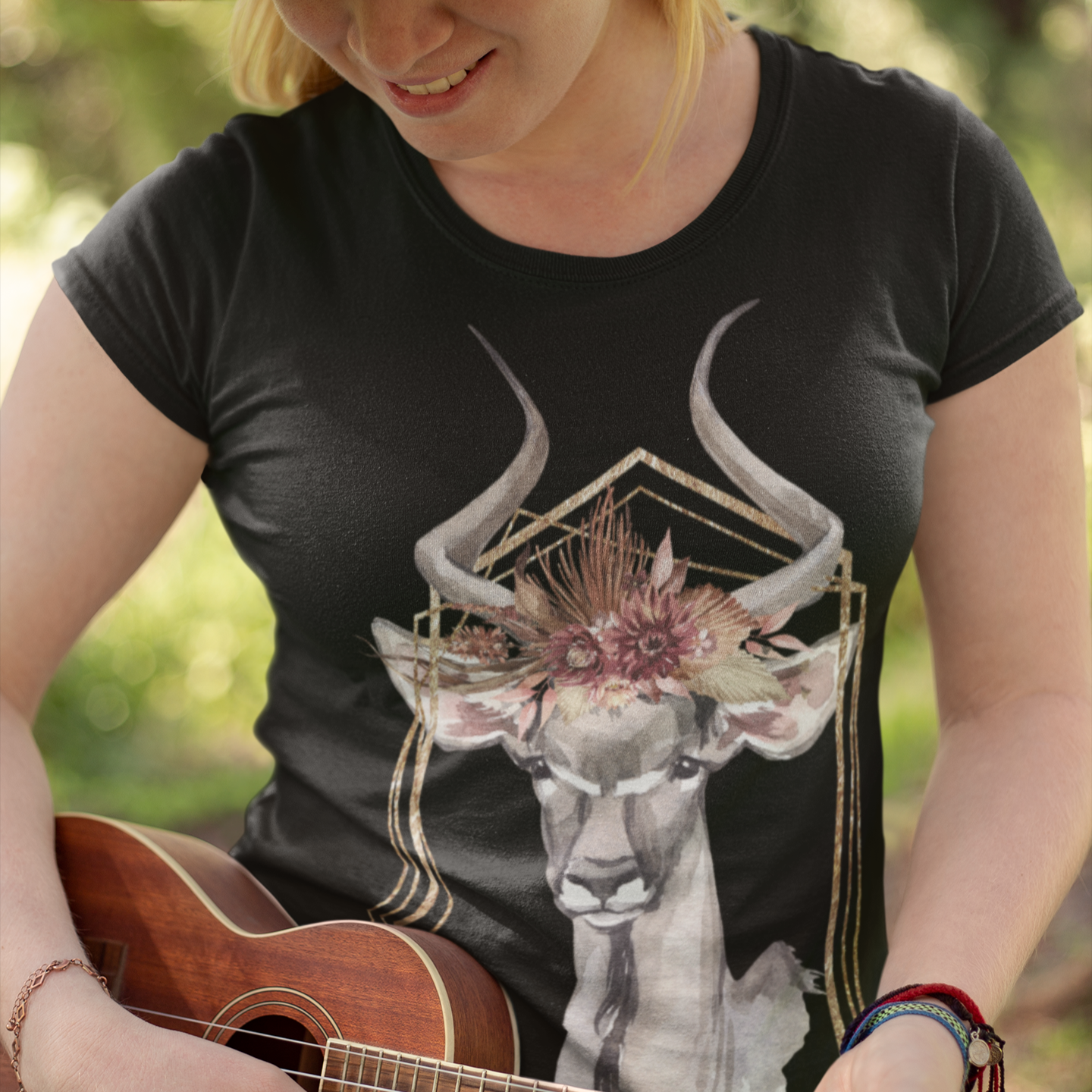 Person playing a ukulele wearing a black t-shirt with a deer design outdoors.