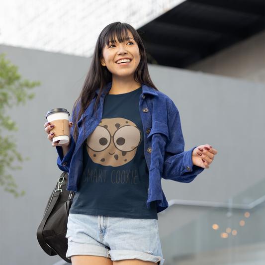 Woman holding a coffee cup, wearing a blue shirt with a cookie design and denim jacket, standing outdoors.