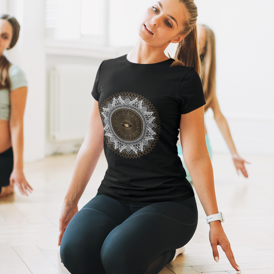 Woman in a black t-shirt with a mandala design sitting on the floor in a bright room.