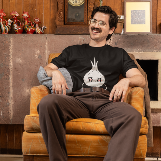 Man sitting in an armchair wearing a black t-shirt with a graphic design, in a room with wooden walls and decorative items.