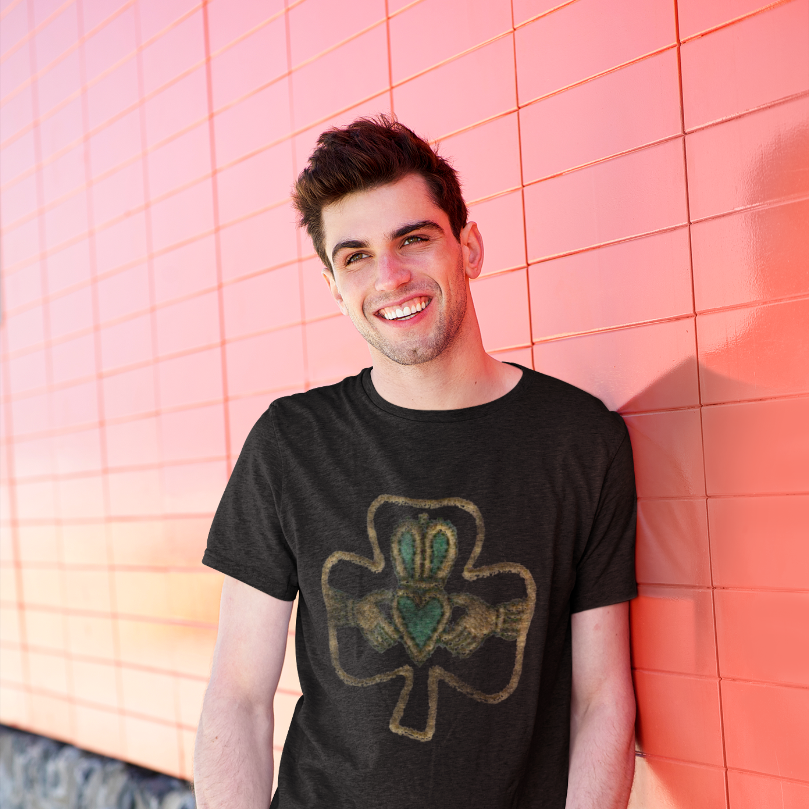 Man wearing a black t-shirt with a shamrock design against a pink tiled wall.
