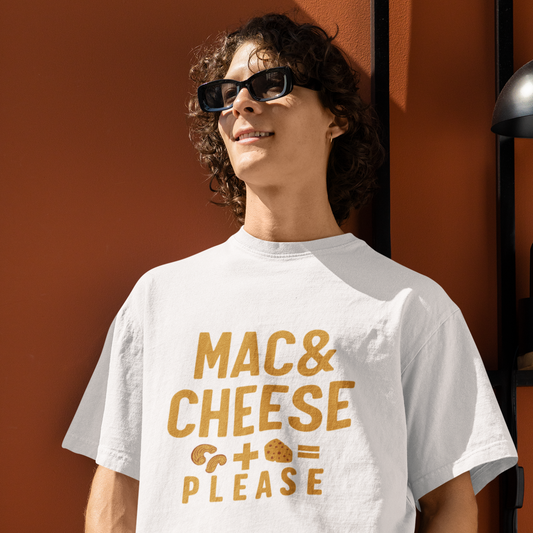 Person wearing a white t-shirt with 'MAC & CHEESE PLEASE' text in gold, standing against an orange wall.