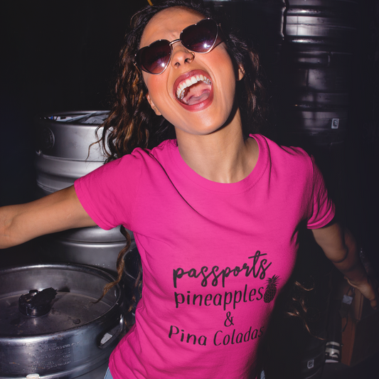Person wearing a pink t-shirt with text standing among metal barrels.