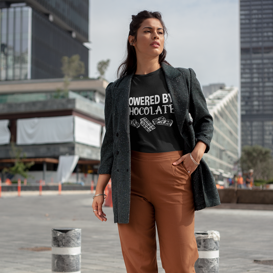 Woman wearing a black t-shirt with text, brown pants, and a dark blazer in an urban setting.