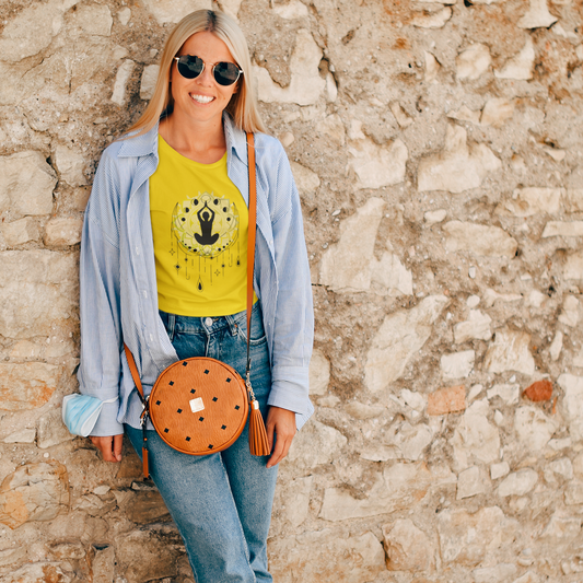 Woman wearing a yellow t-shirt with a graphic design, blue jeans, and sunglasses, standing against a stone wall.