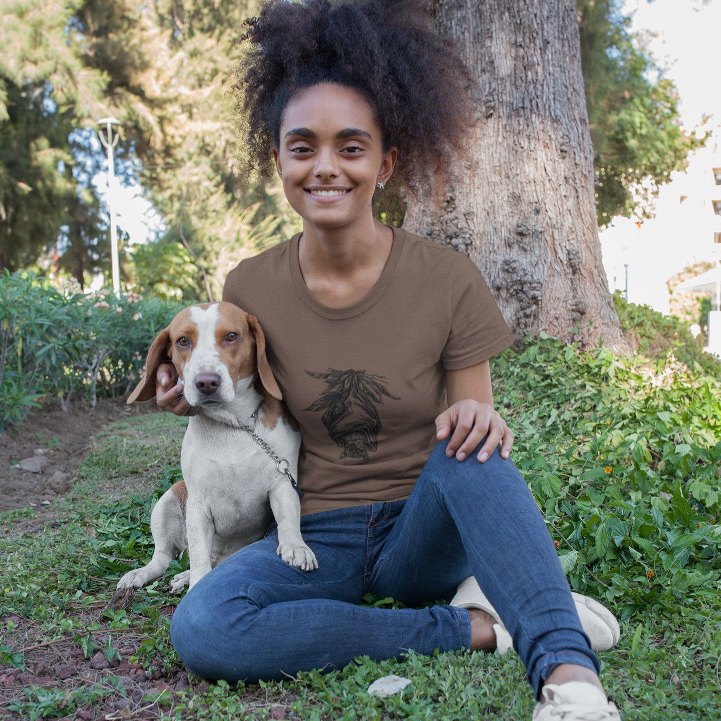 Woman sitting on grass with a dog, wearing a brown t-shirt with a graphic design.