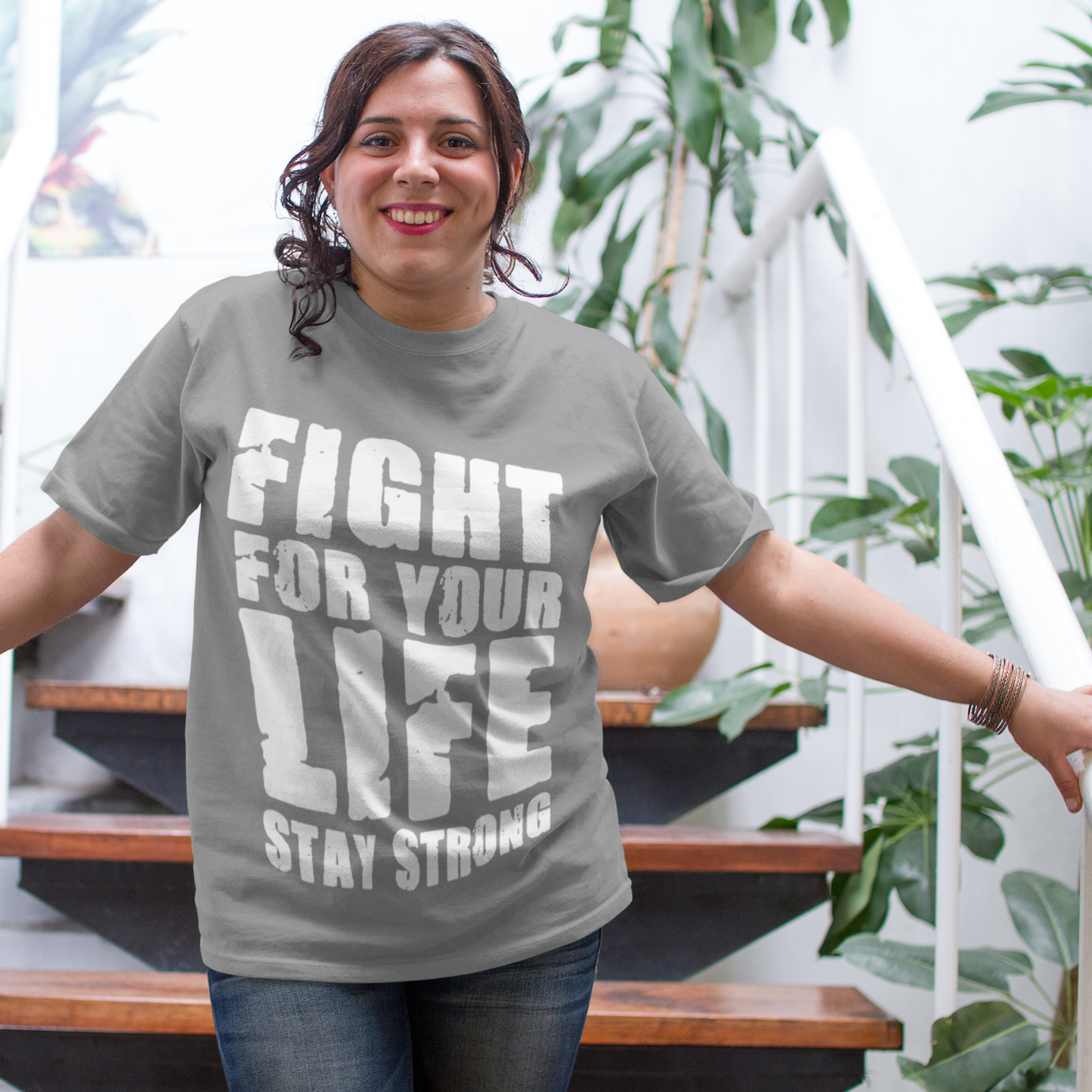 Person wearing a gray t-shirt with motivational text, standing in an outdoor setting with plants.
