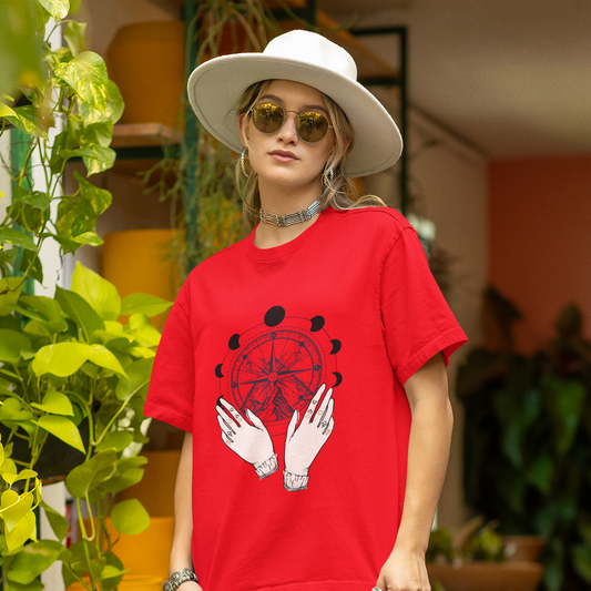 Person wearing a red t-shirt with a graphic design, standing outdoors with plants in the background.
