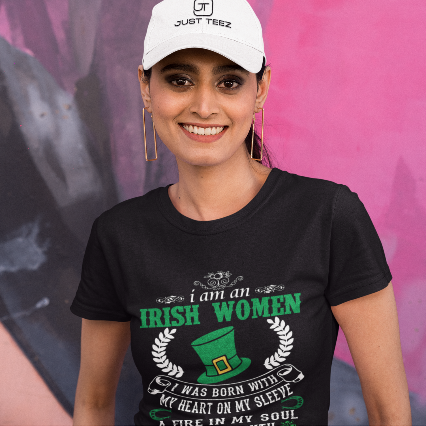 Woman wearing a black t-shirt with text and a white cap in front of a colorful mural.