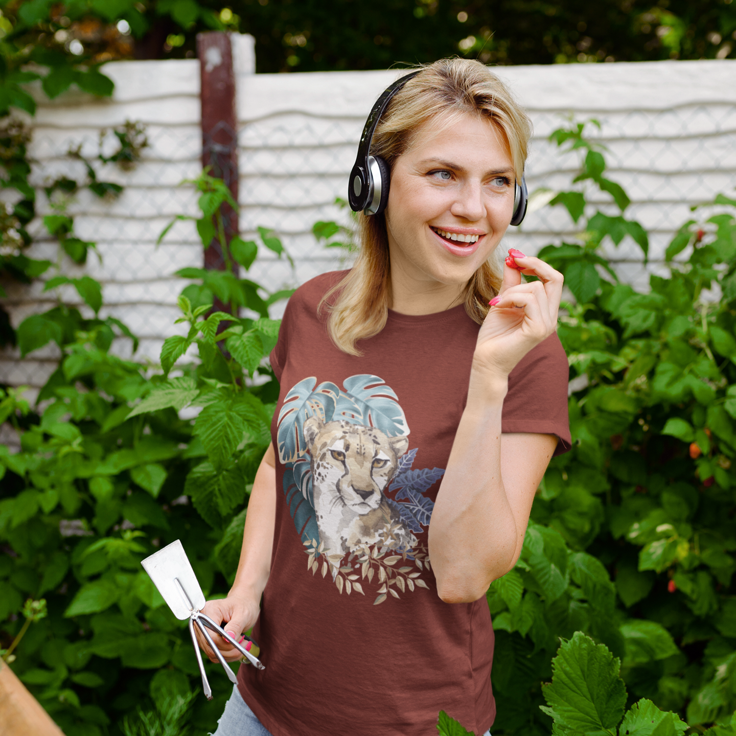 Woman standing in a garden wearing headphones and holding a smartphone.