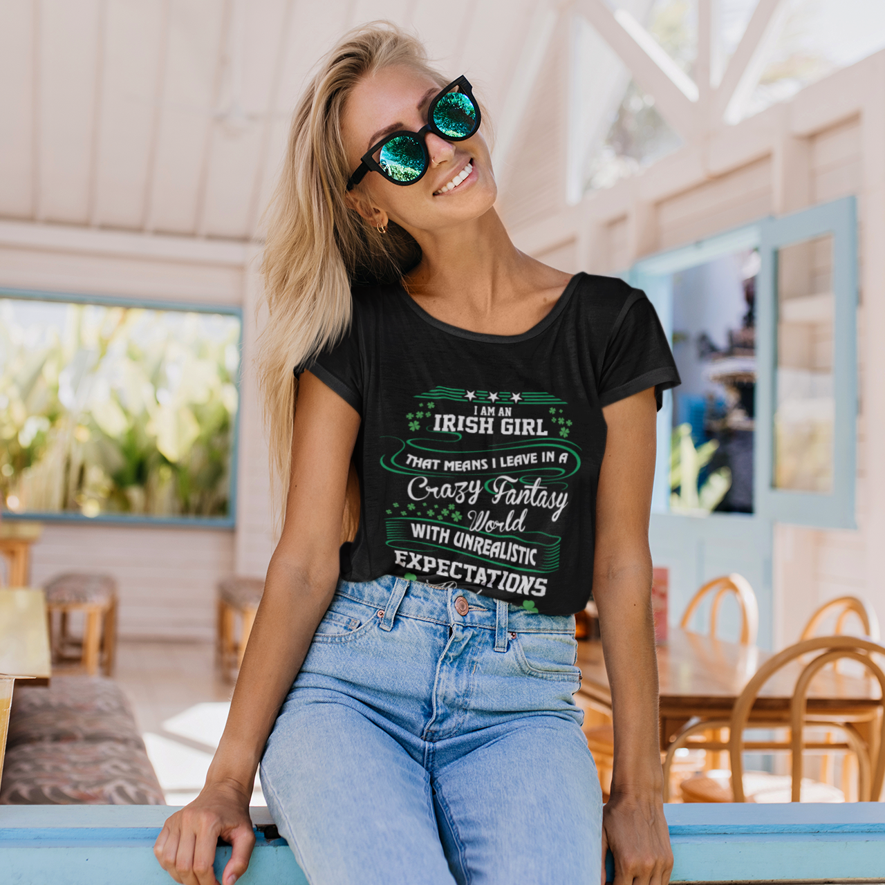 Woman wearing a black t-shirt with text, sunglasses, and blue jeans in a casual setting.