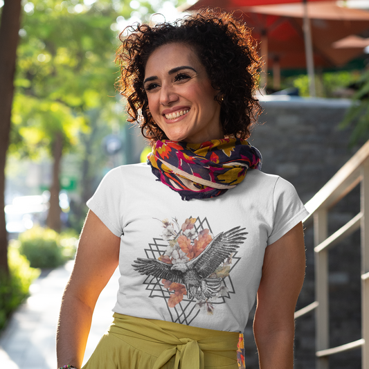 Woman wearing a white t-shirt with an eagle design and a colorful scarf outdoors.