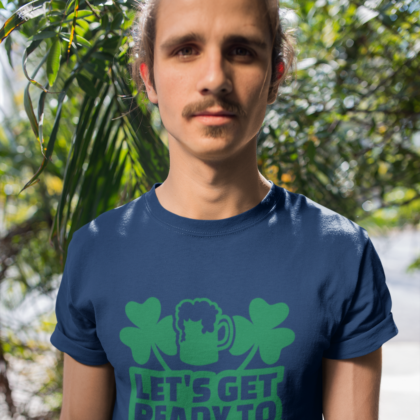 Man wearing a blue t-shirt with green shamrock design and text outdoors.
