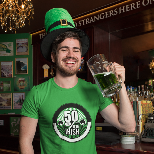 Man in a green shirt with a '50% Irish' design, holding a mug of green beer in a bar.