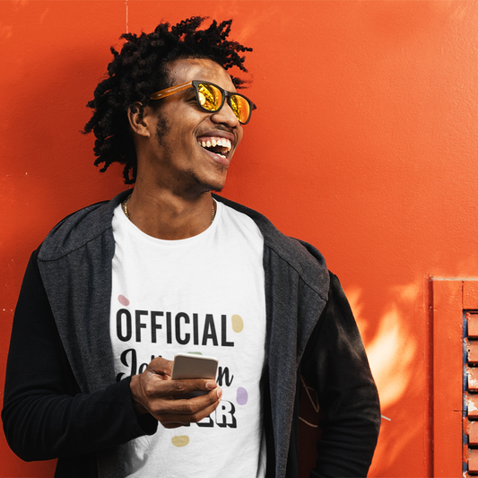 Man wearing a white t-shirt with text, holding a phone, against an orange wall.