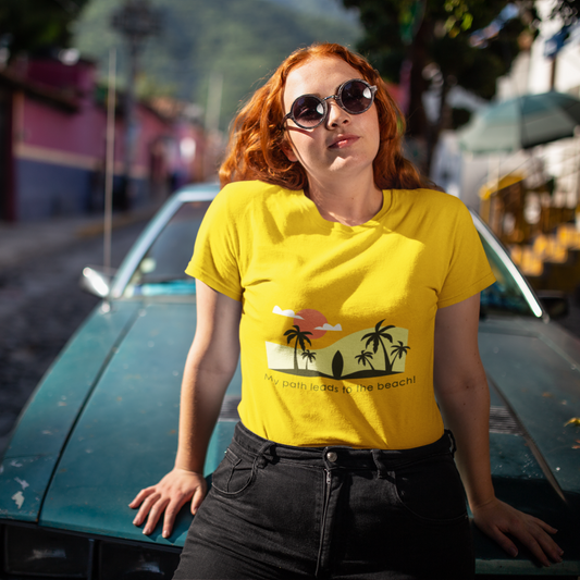 Woman wearing a yellow t-shirt with a palm tree design, standing next to a vintage car on a street.