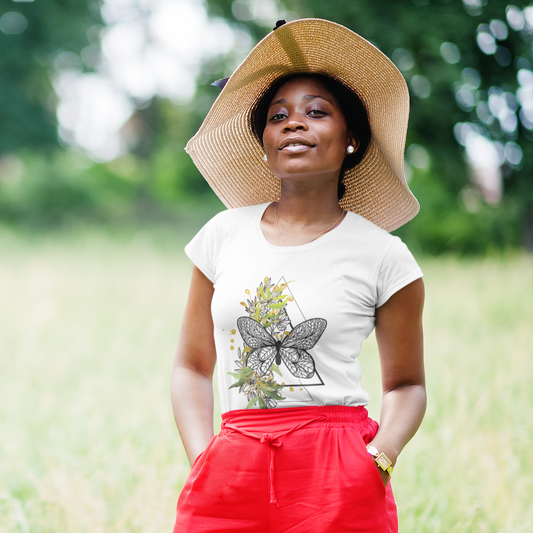 Woman wearing a white t-shirt with a butterfly design and red pants, standing in a grassy field.