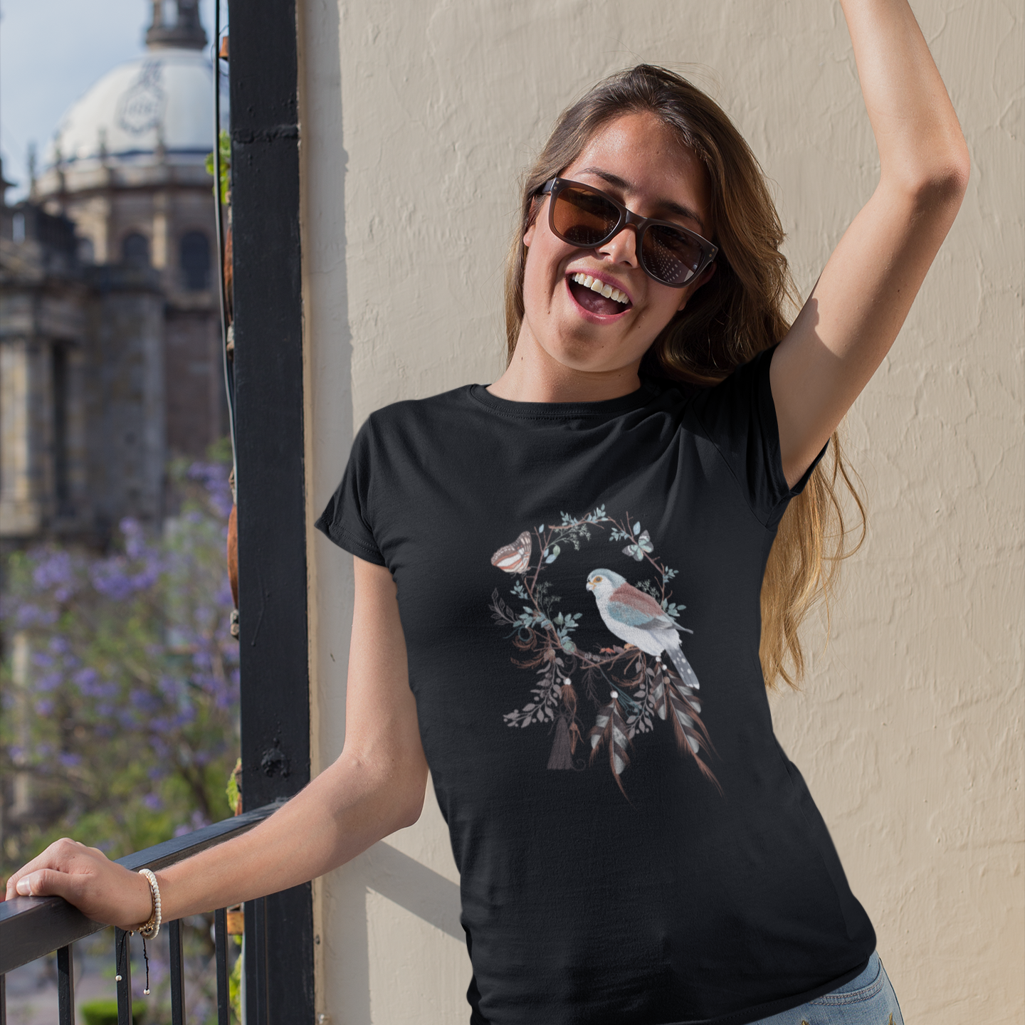 Woman wearing a black t-shirt with a bird design, standing on a balcony with a cityscape background.