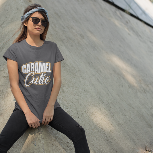 Person wearing a gray t-shirt with 'Caramel Cutie' text, sitting on a concrete surface.