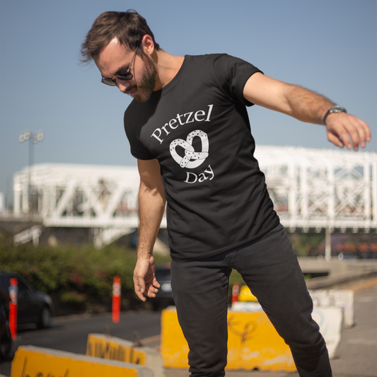 Man wearing a black t-shirt with 'Pretzel Day' design, balancing on a yellow barrier.